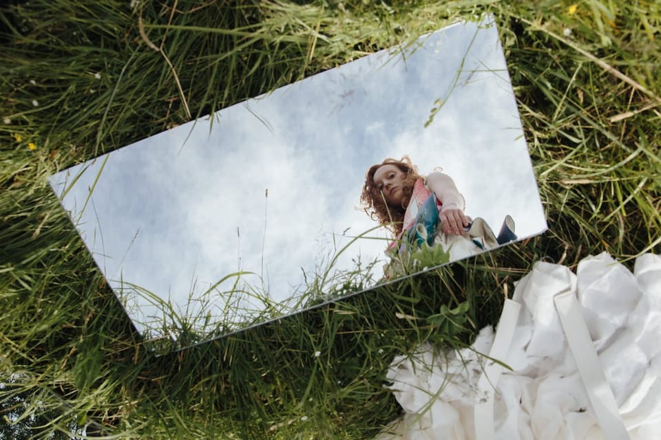 A woman gazes into a mirror outdoors, symbolizing introspection and self-awareness.