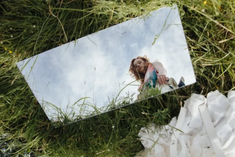 A woman gazes into a mirror outdoors, symbolising introspection and self-awareness.